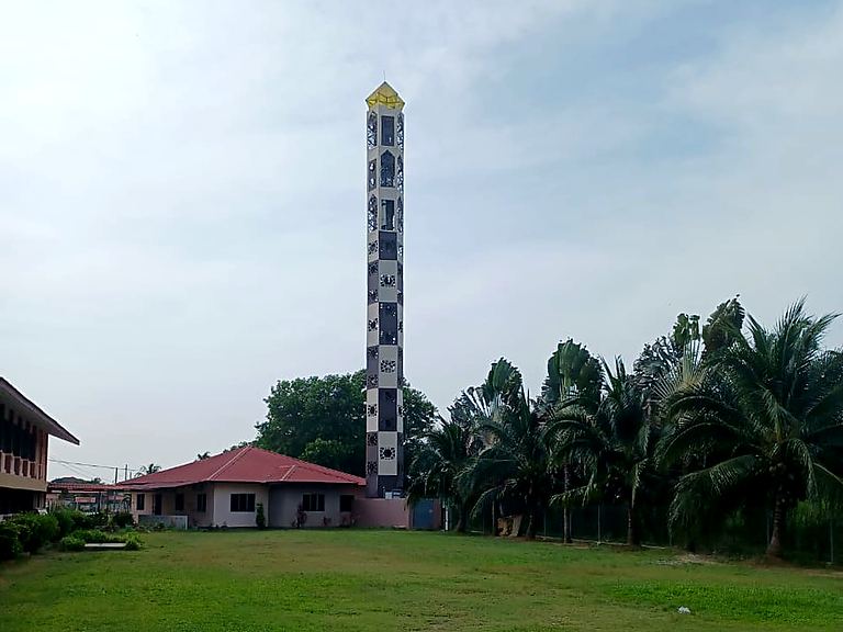 Minaret-style structure at the edge of an open field beside a community building