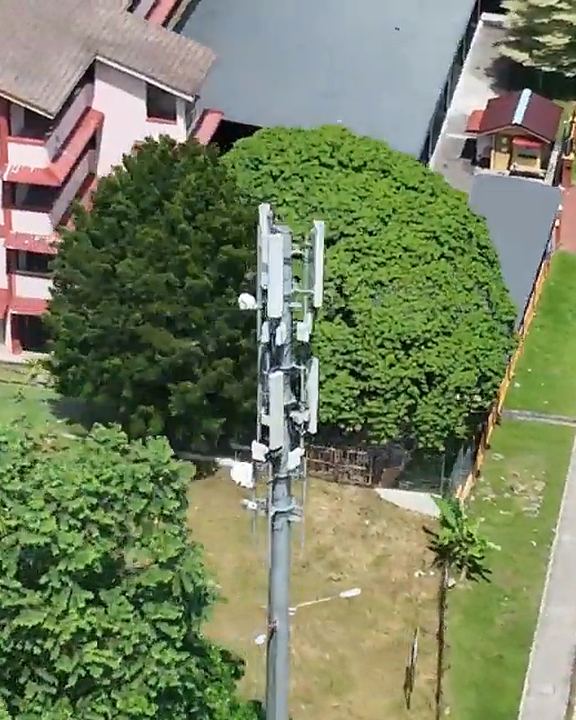 Aerial view of a monopole beside trees and a car park